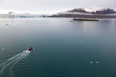 A motorized boat heads for a rocky island near ice floes and mountains in the distance.