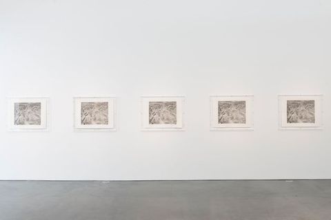 Installation. Five silvery black and white photographs are contained in acrylic boxes hung on a gallery wall. The images show a mine.
